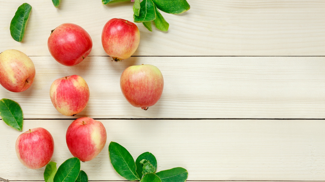 Красные яблоки с зелеными листьями на деревянном столе 