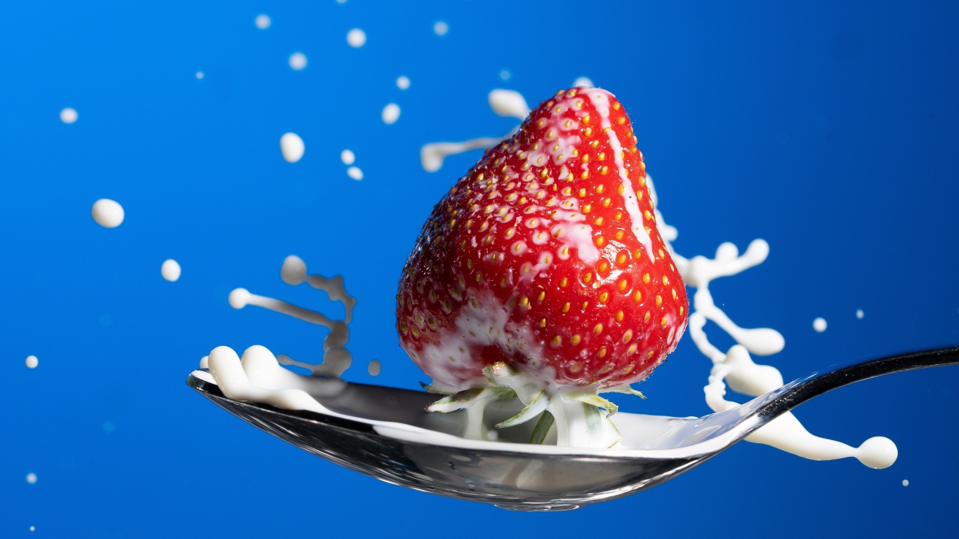 Ripe red strawberries in a spoon of milk on a blue background