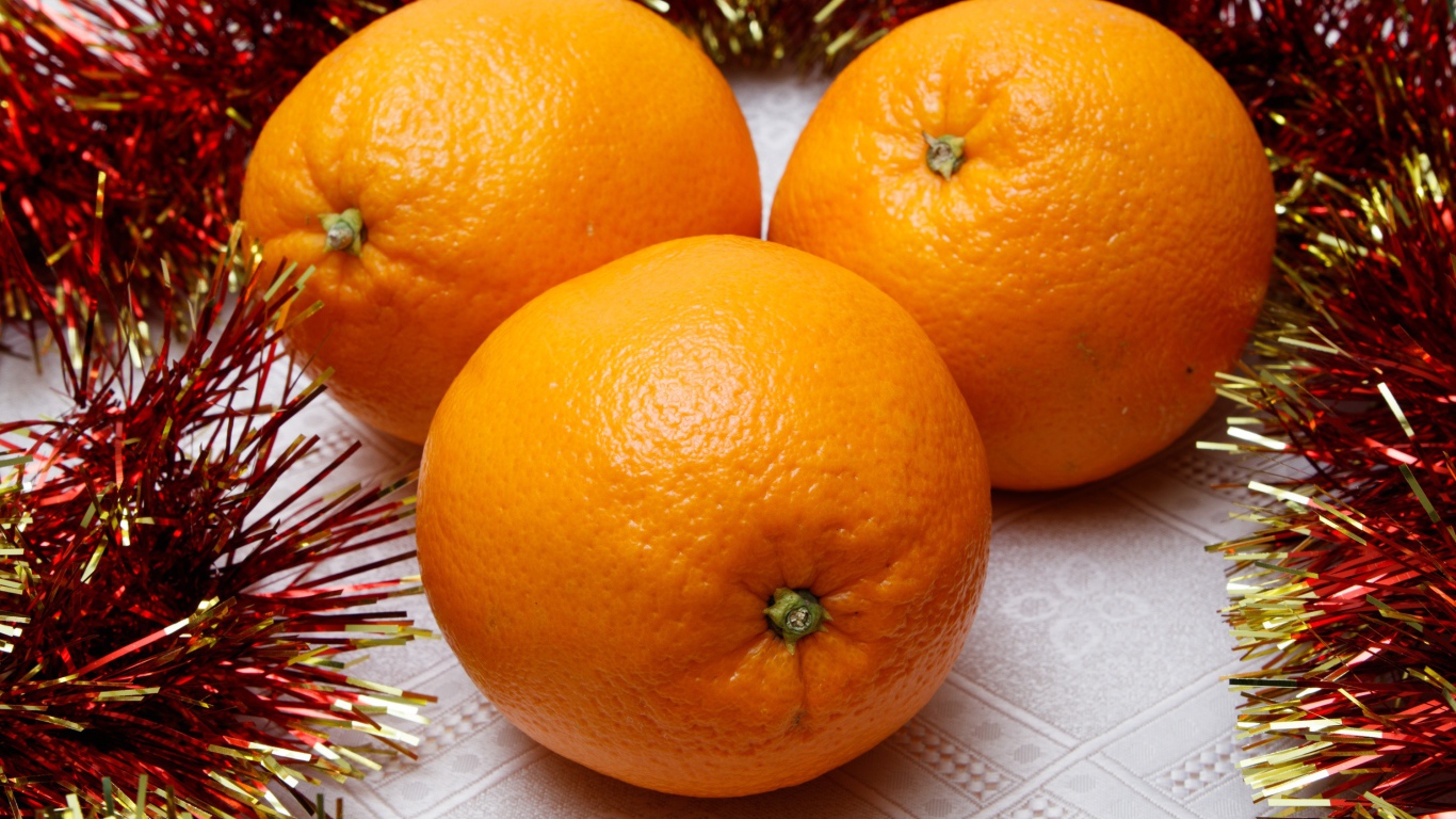 Три больших апельсина на столе с мишурой 