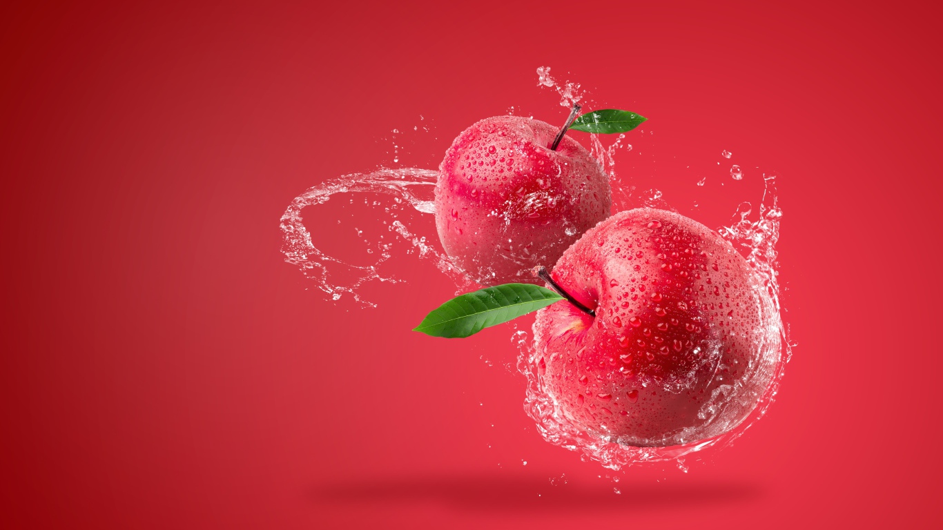 Два яблока в брызгах воды на красном фоне