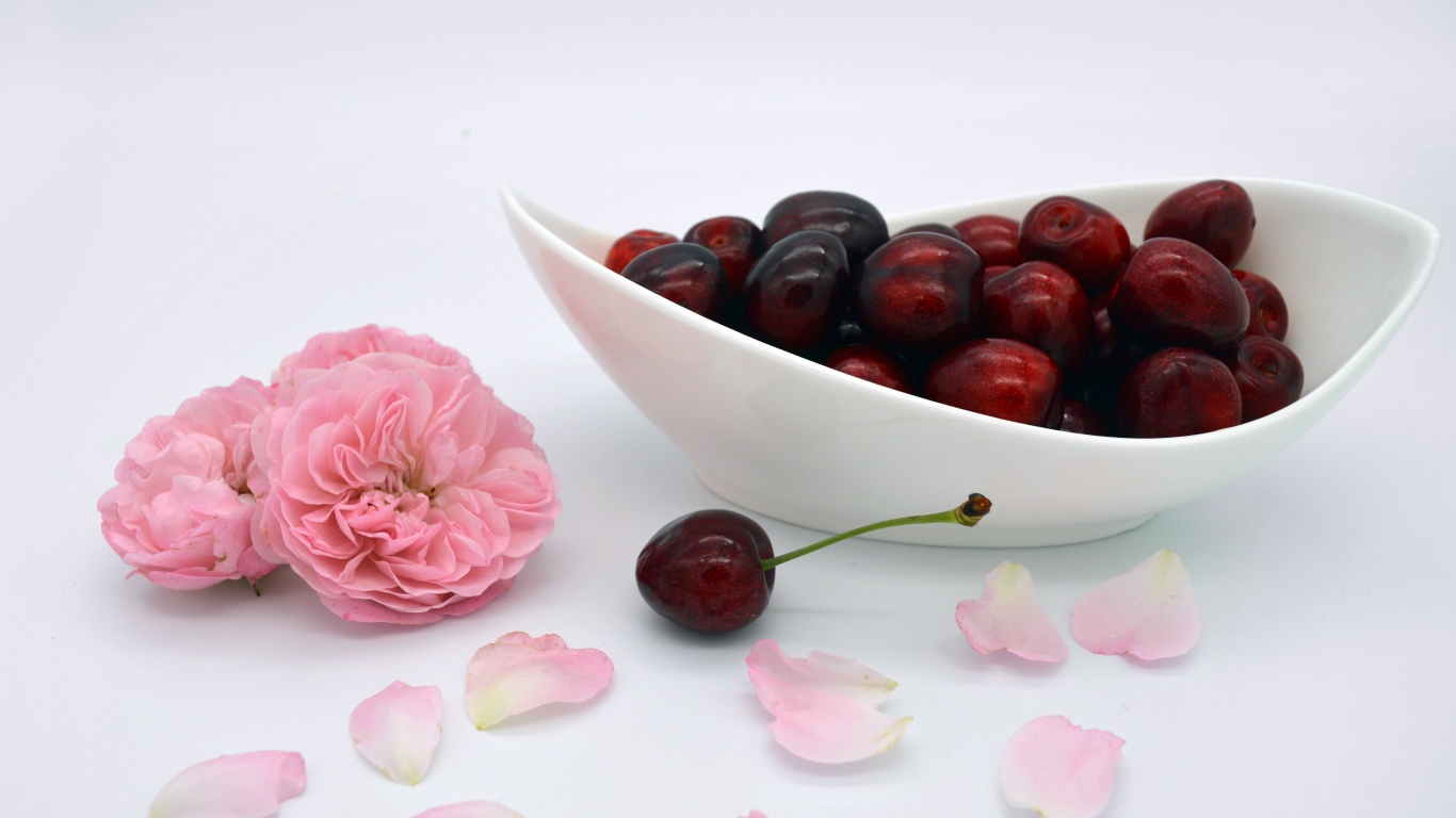 White plate with red cherries on the table with flowers