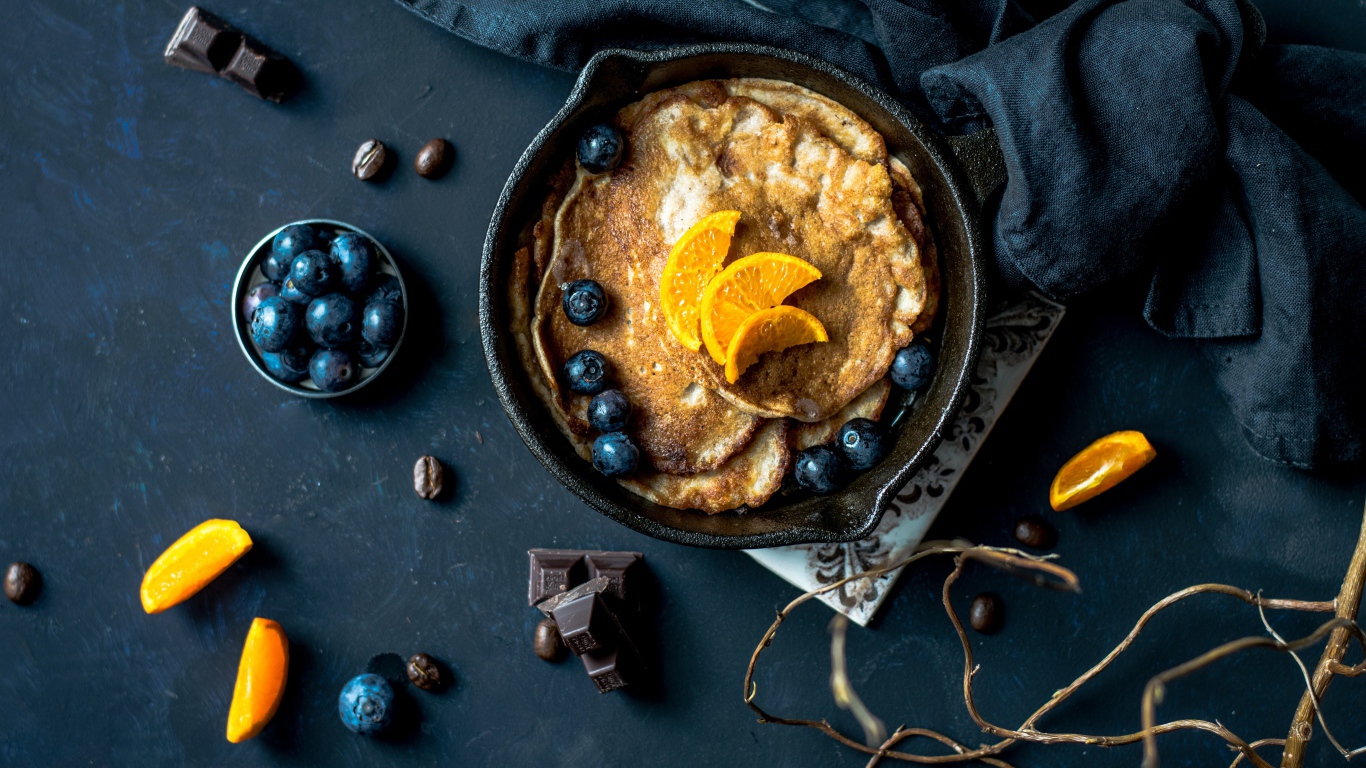 Блины с ягодами черники и апельсинами на столе 