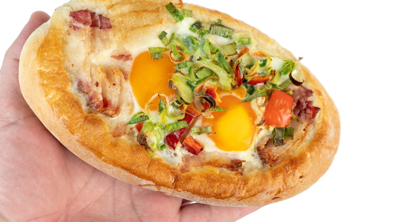 Вкусный свежий хачапури с яйцом и беконом в руке