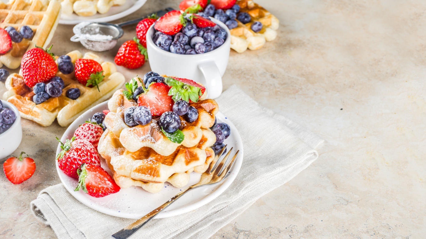 Вкусные сладкие вафли на тарелке с ягодами и сахарной пудрой 