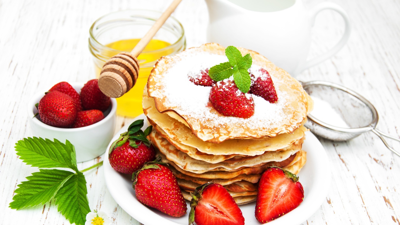 Тонкие блины с сахарной пудрой и ягодами клубники на столе с молоком и медом