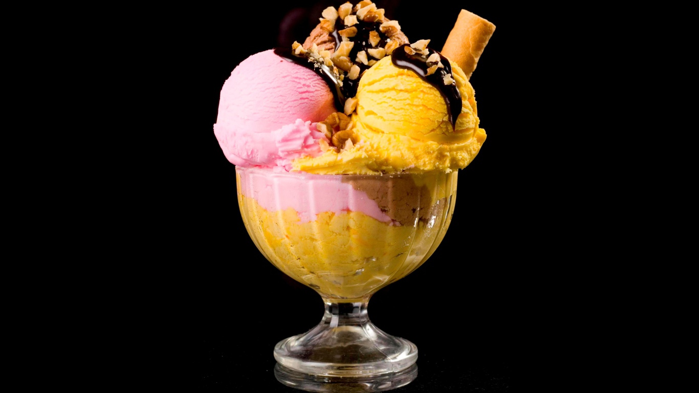 Шарики фруктового мороженого в креманке с орехами и шоколадом на черном фоне