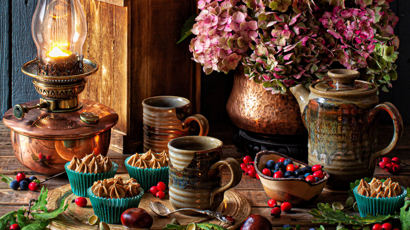 Кексы с кремом на столе с ягодами, цветами и лампой 