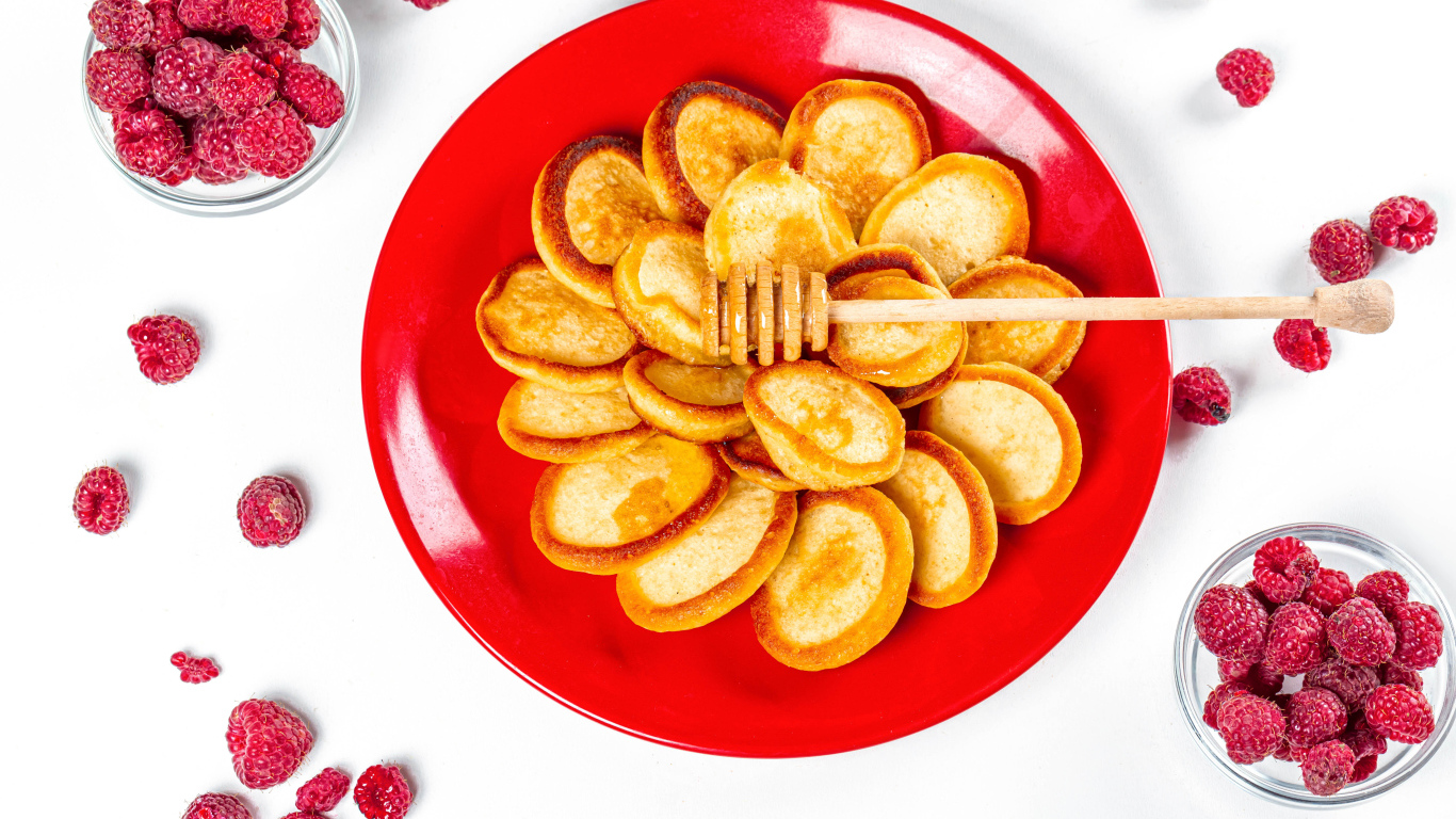 Оладьи на красной с медом на красной тарелке на столе с ягодами малины