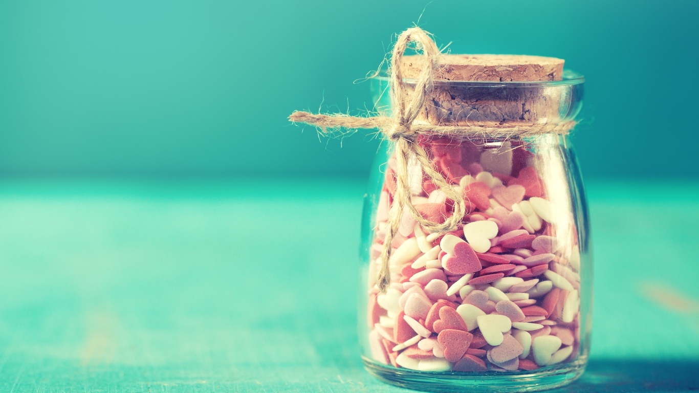 Стеклянная банка с маленькими конфетами в форме сердца на голубом фоне