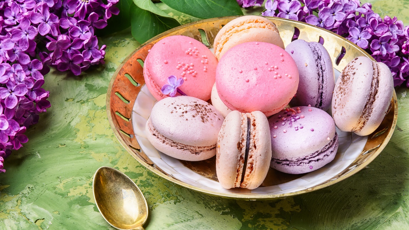 Разноцветный десерт макарон в тарелке на столе с цветами сирени 