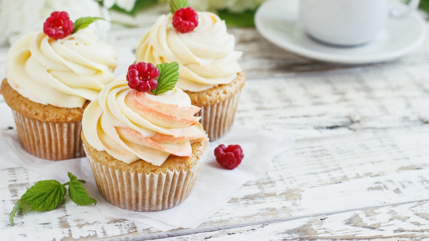 Три кекса с кремом на столе с чашкой кофе