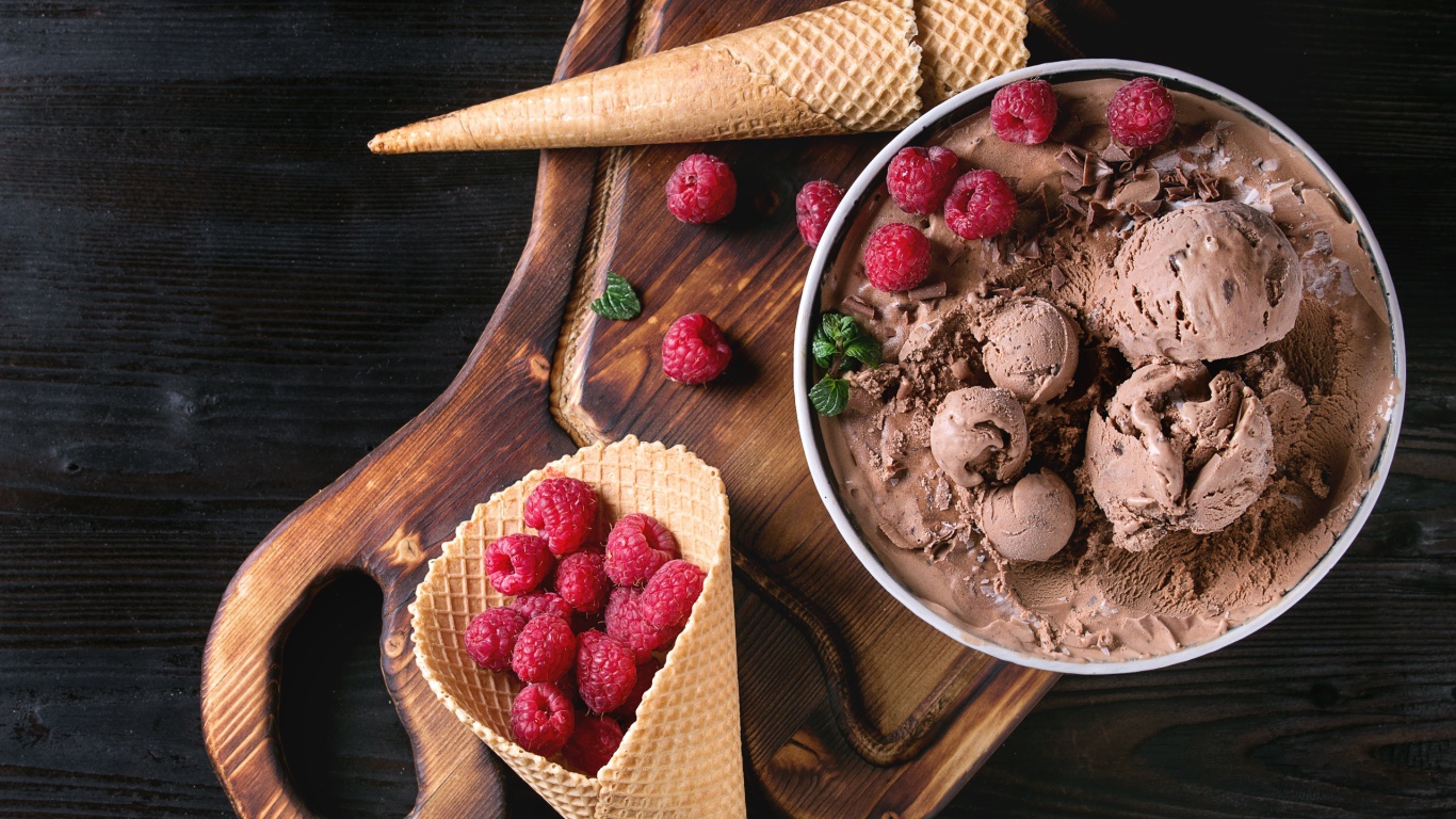 Вафельный рожок с шоколадным мороженым и ягодами малины на столе