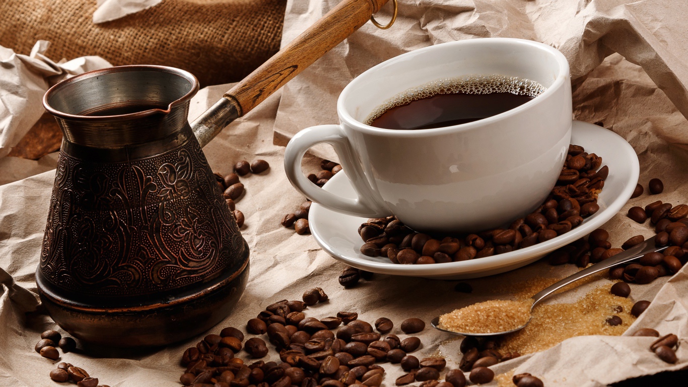 Чашка горячего кофе на столе с туркой, зернами и коричневым сахаром