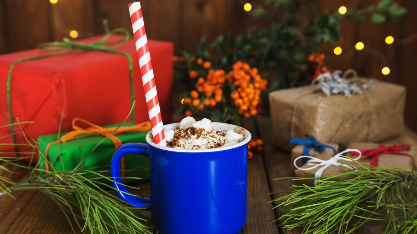 Blue cup of hot chocolate with marshmallows on a table with fir branches and gifts.
