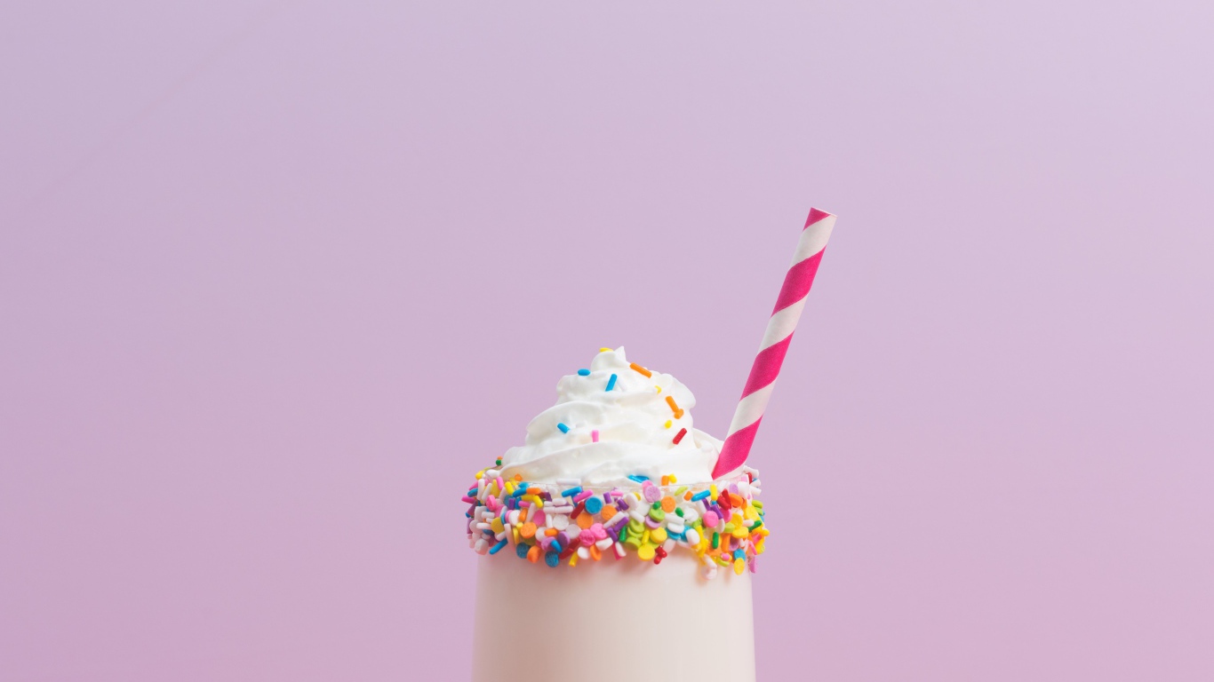 Коктейль  в стакане со взбитыми сливками на розовом фоне