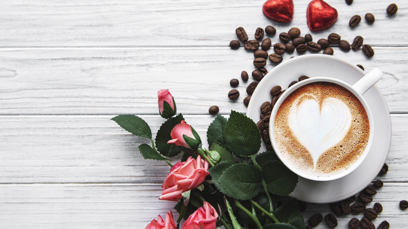 Чашка кофе с рисунком на пене на столе с букетом роз, зернами и конфетами