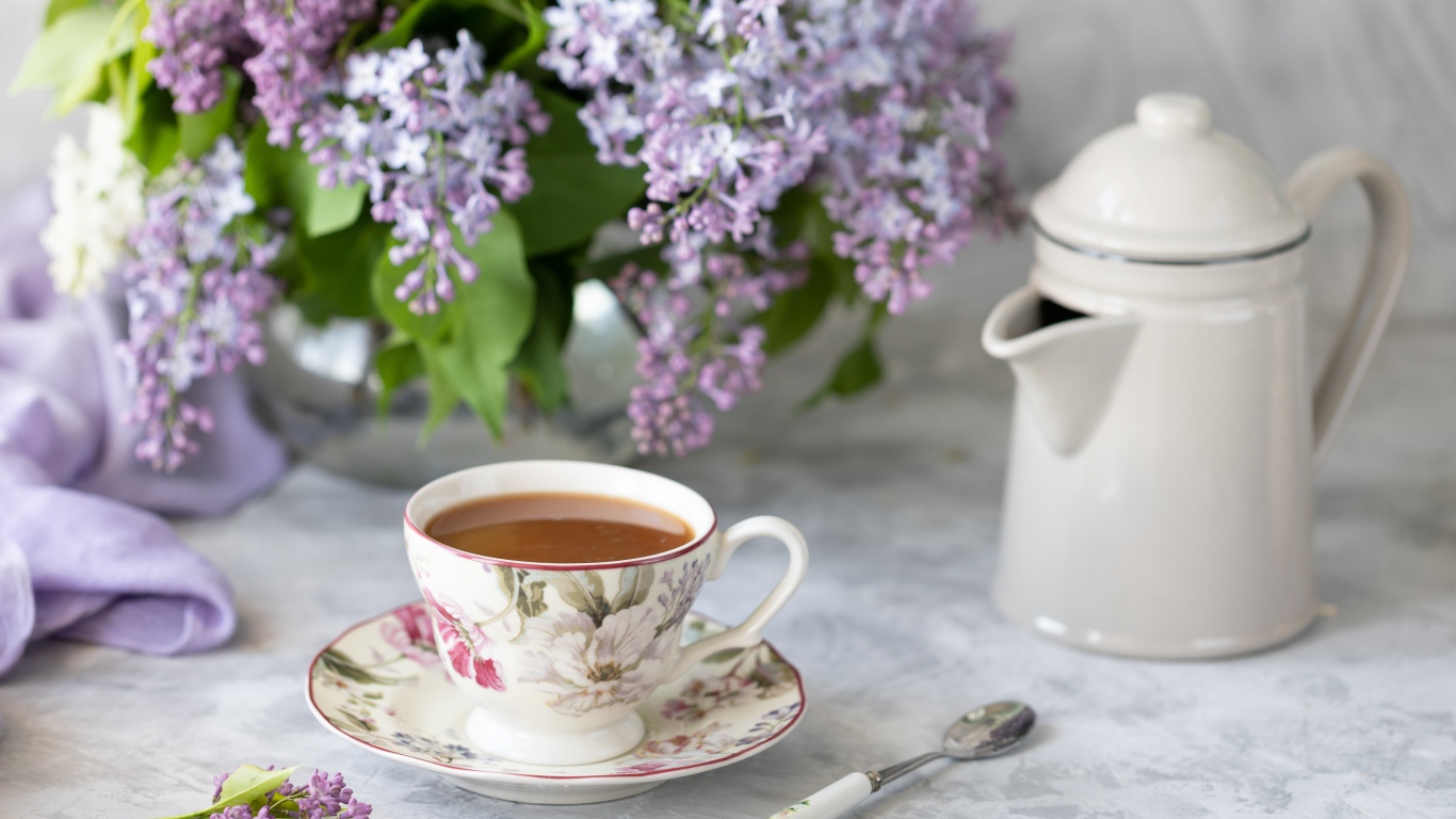 Чашка кофе с чайником на столе с букетом сирени 