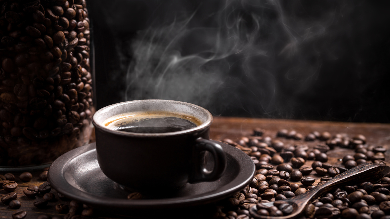 Чашка горячего ароматного кофе на столе с зернами и ложкой