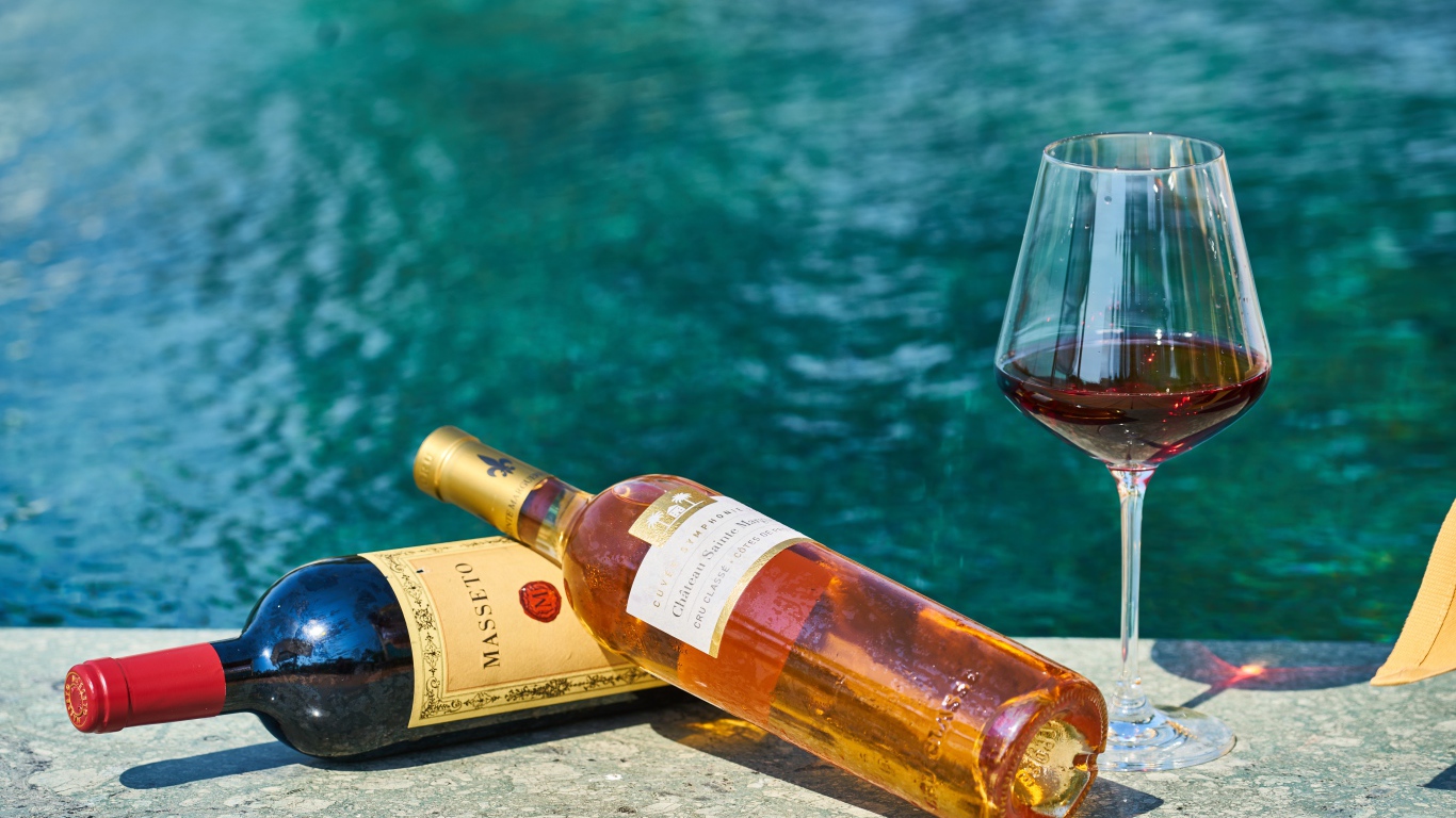 Две бутылки вина и бокал у бассейна
