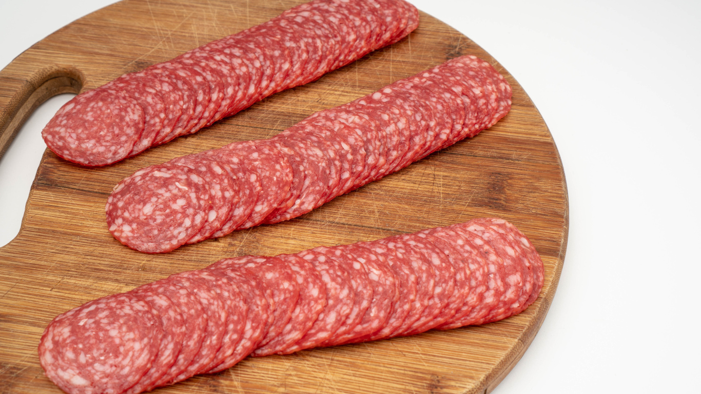 Колбаса тонко нарезана на разделочной доске 