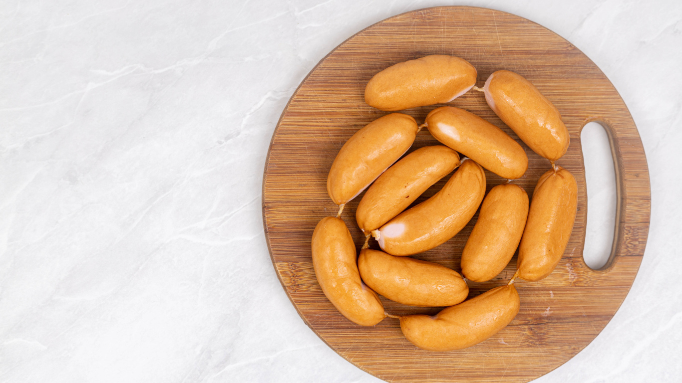 Копченые сардельки на деревянной доске на сером фоне