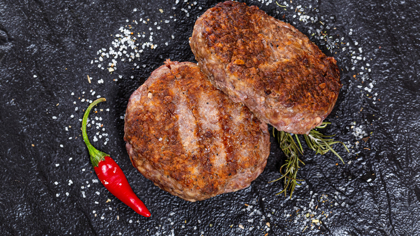 Две котлеты на черной поверхности с красным перцем