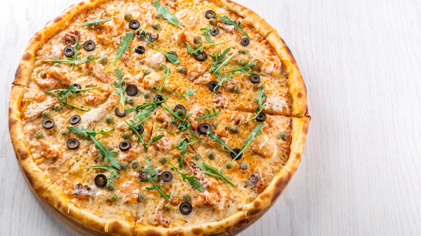 Пицца с морепродуктами, рукколой и оливками на столе 