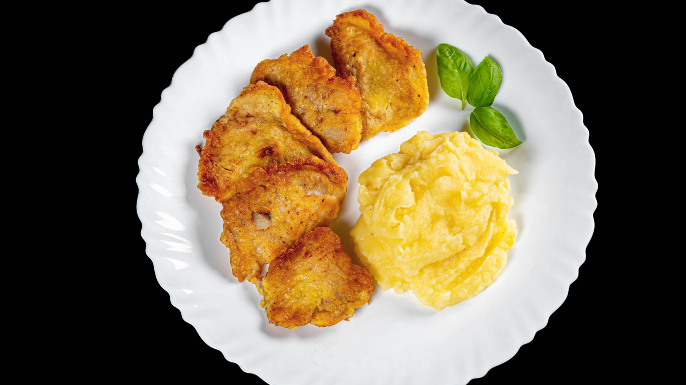 Куски жареной рыбы с картофельным пюре в тарелке на черном фоне