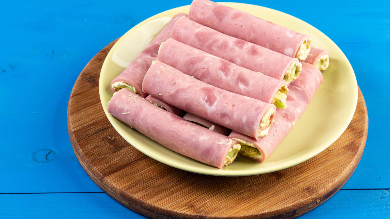 Рулетики из ветчины на тарелке на голубом столе