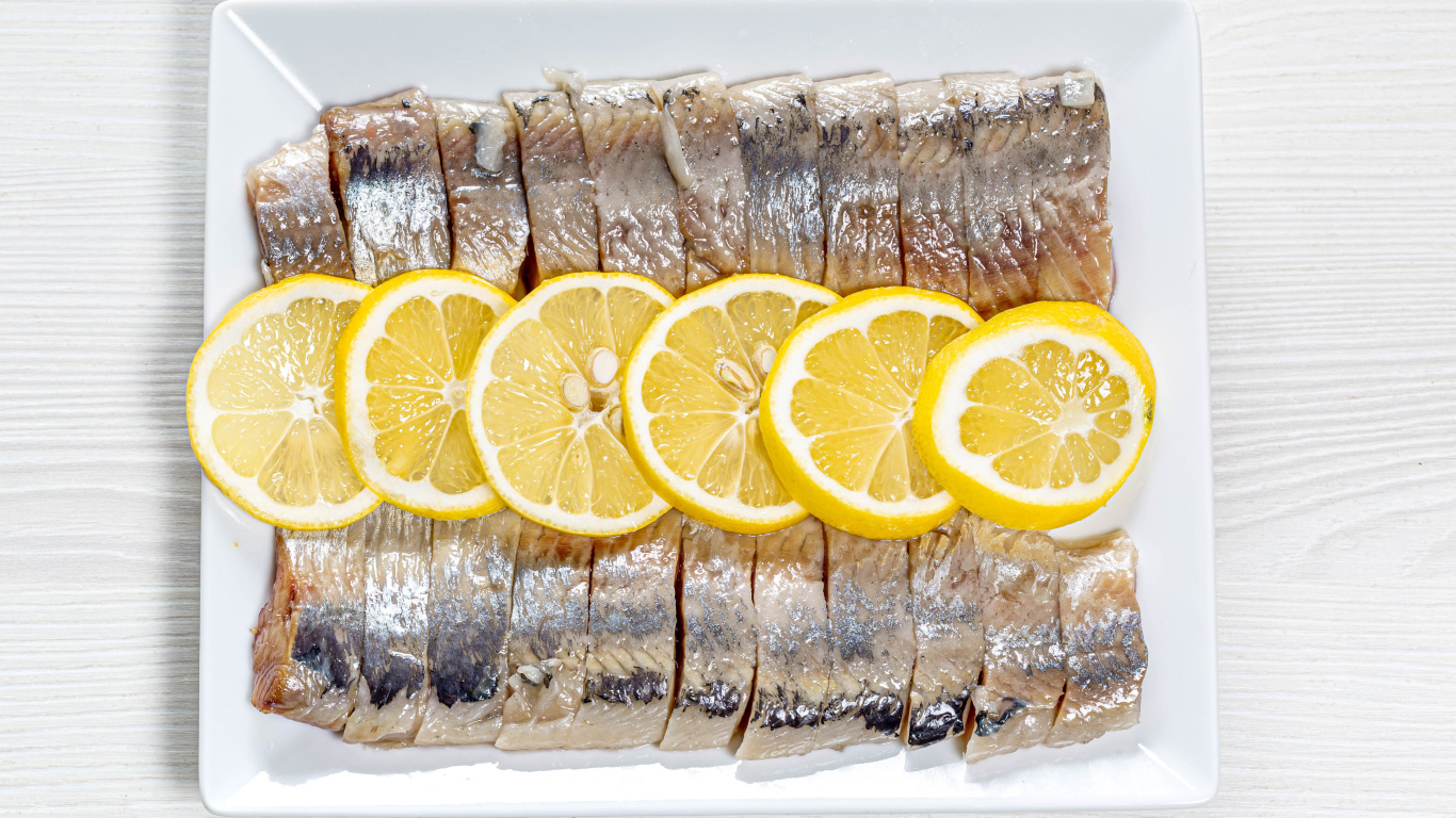 Селедка нарезанная кусочками на белой тарелке с лимоном 