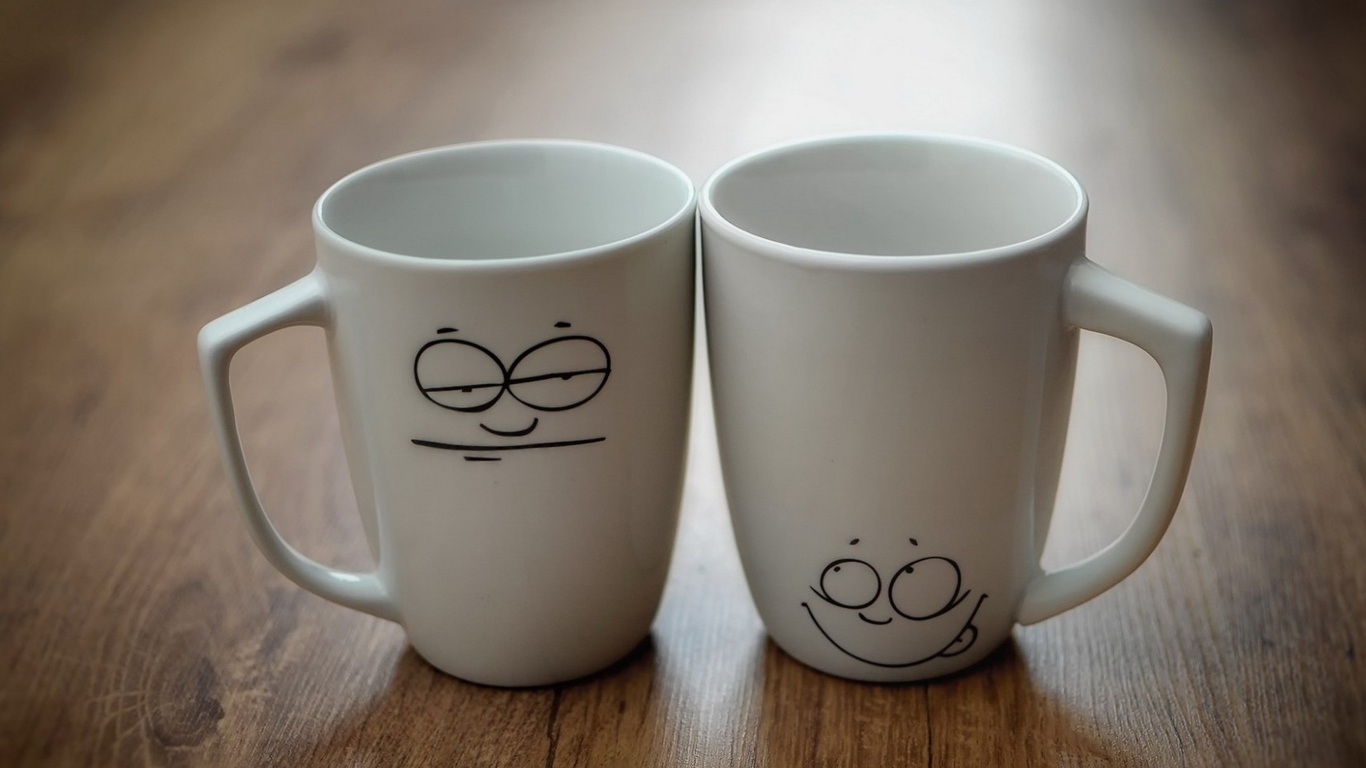Две белые кружки с рисунками на столе 
