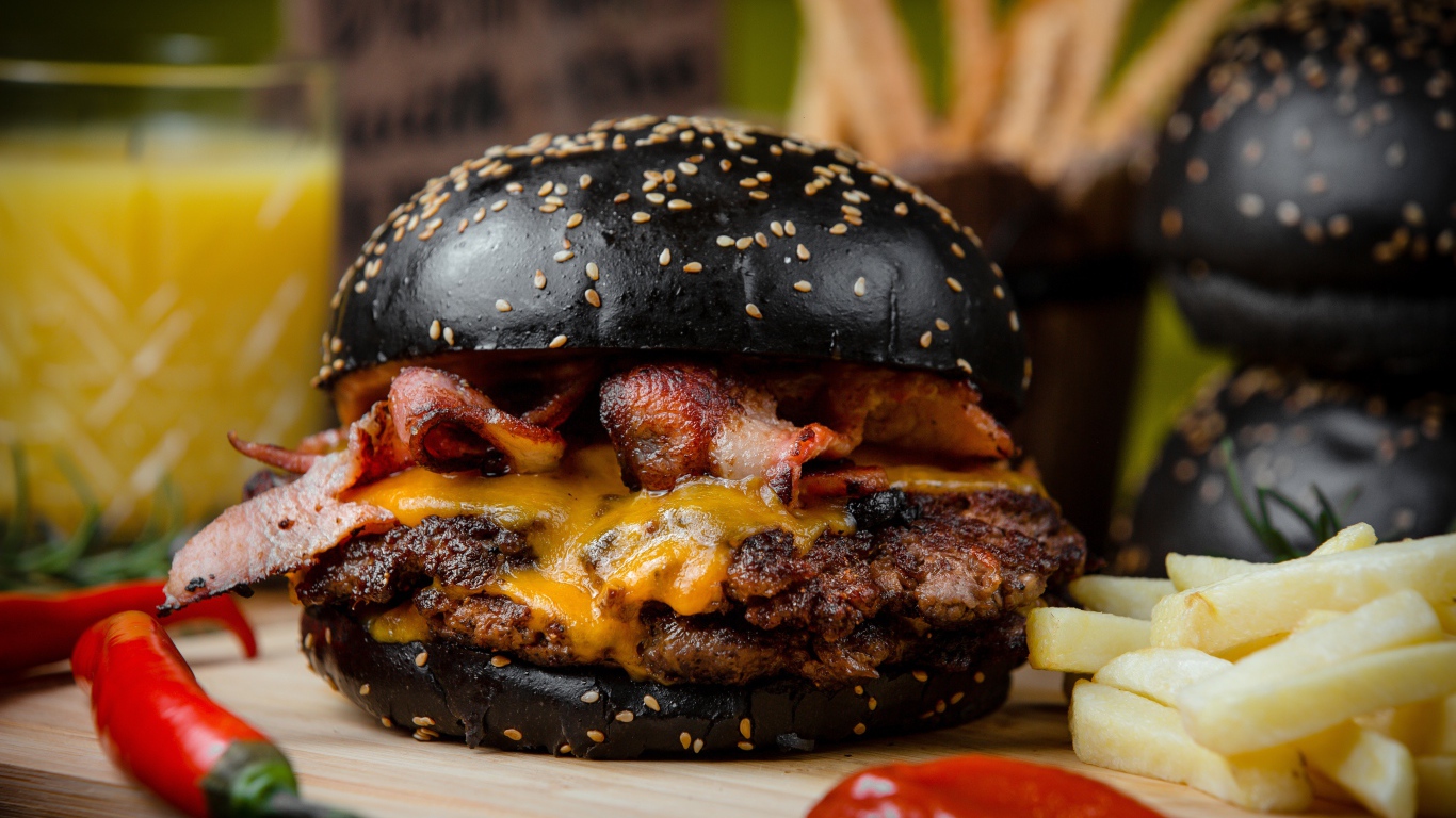 Гамбургер с черной булкой на столе с картофелем фри и красным перцем