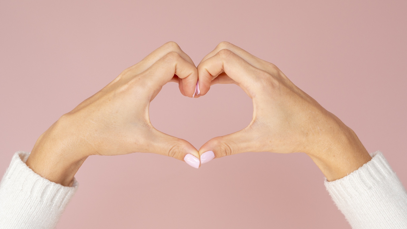 Girl making a heart with her hands on a pink background