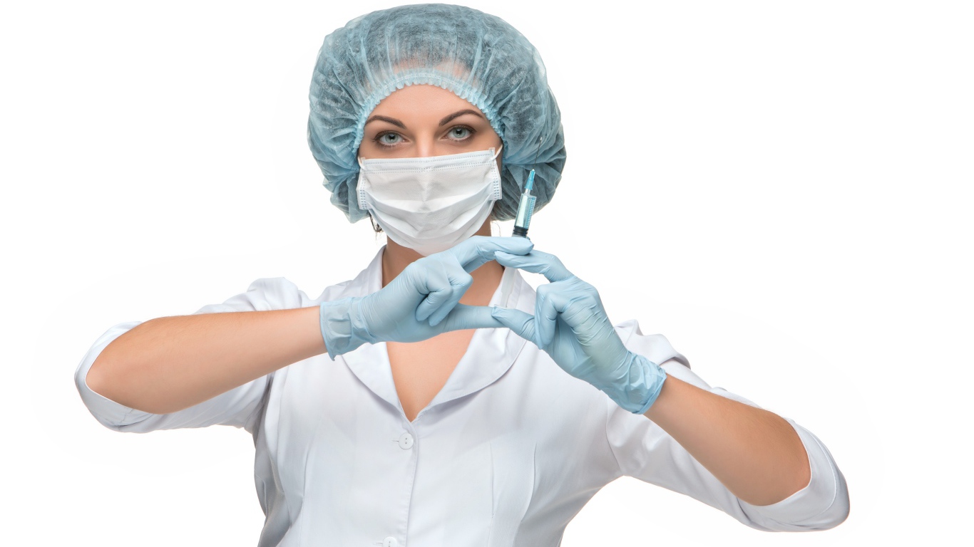 Девушка медсестра в маске со шприцем в руках на белом фоне