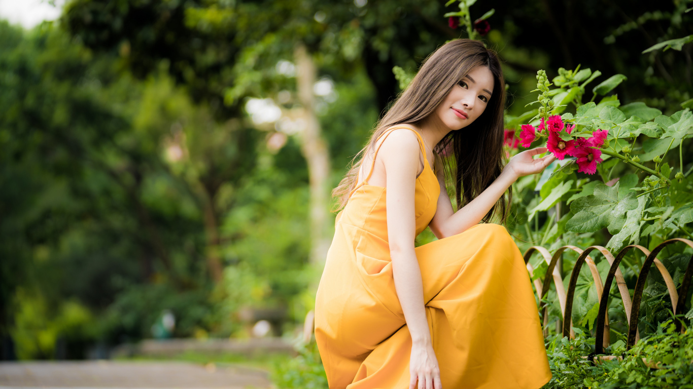 Девушка в желтом платье сидит у цветка мальвы в парке