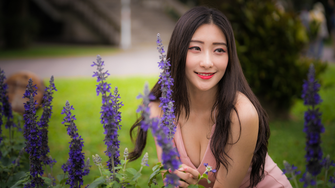 Улыбающаяся азиатка стоит у синих цветов 