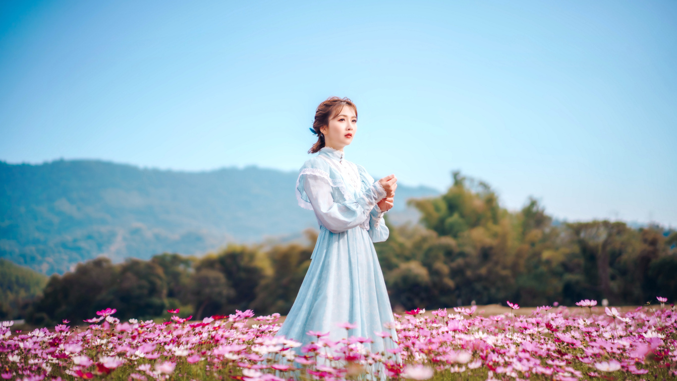 Девушка азиатка в красивом платье идет по полю с цветами космеи