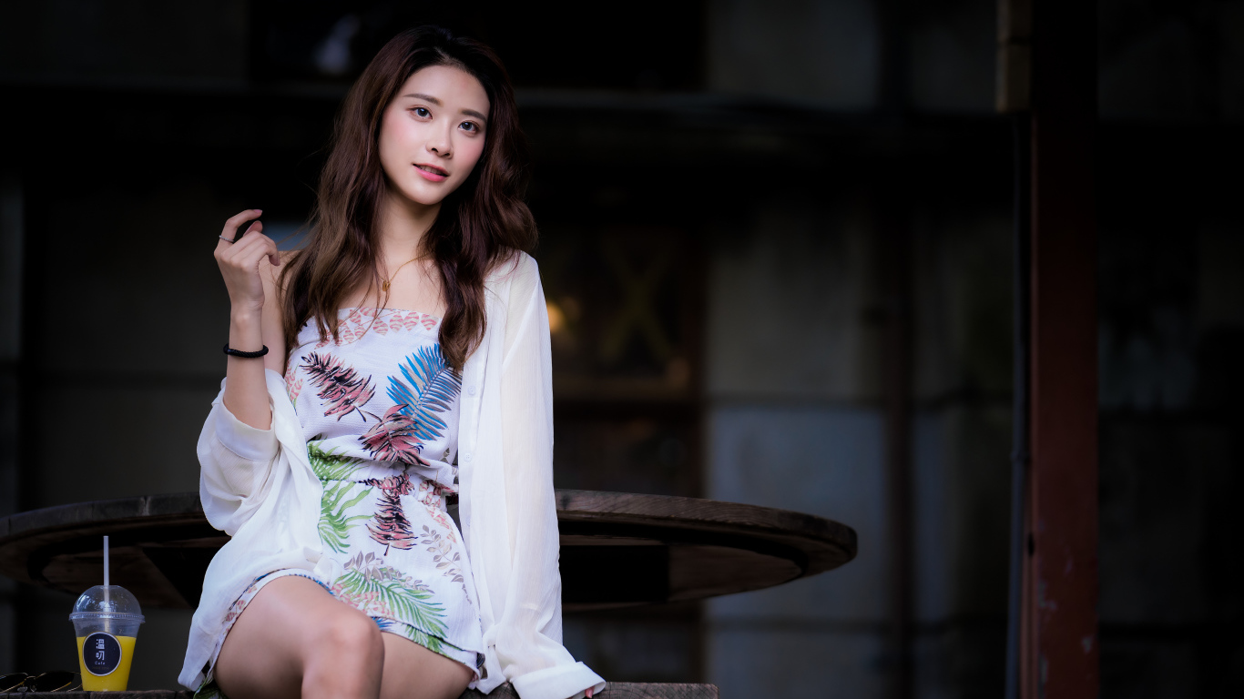 Девушка азиатка в красивом коротком платье сидит на лавке 