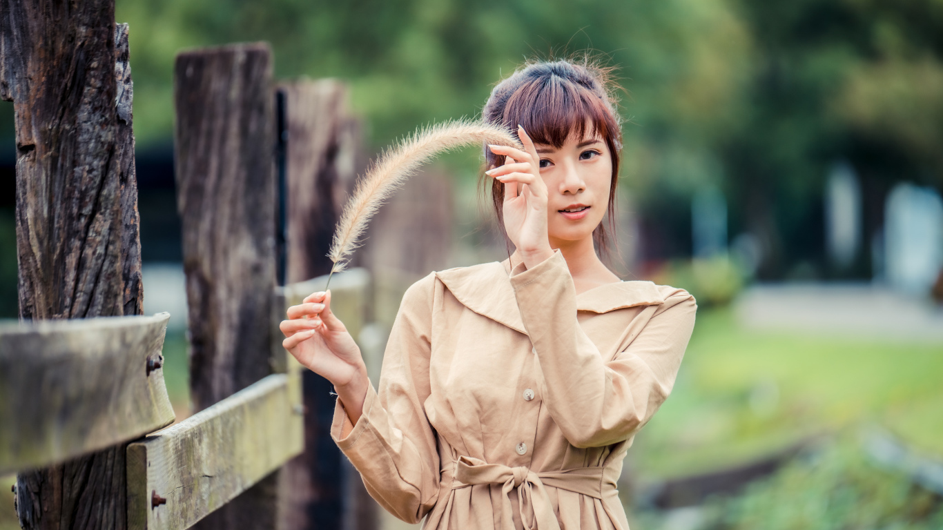 Девушка азиатка в пальто стоит у забора 