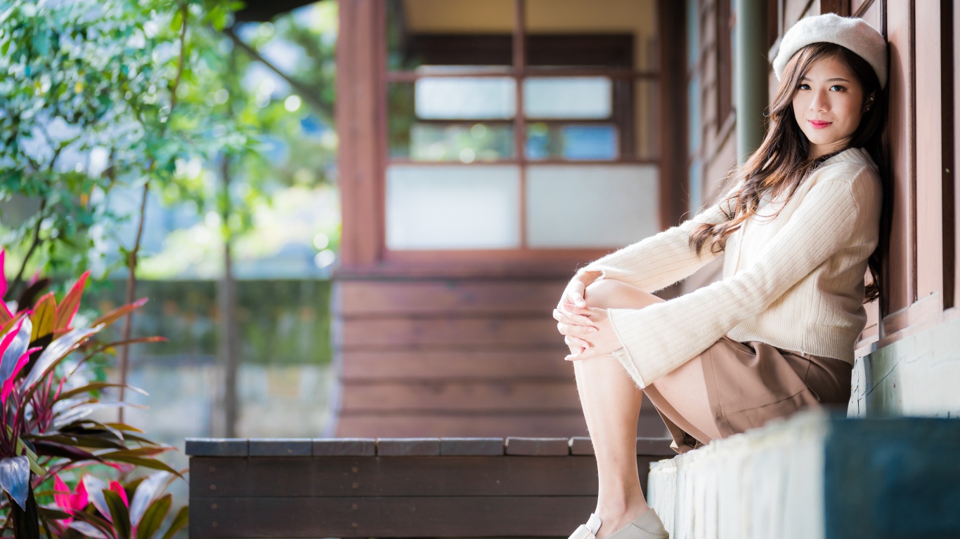 Девушка азиатка в свитере сидит на пороге 