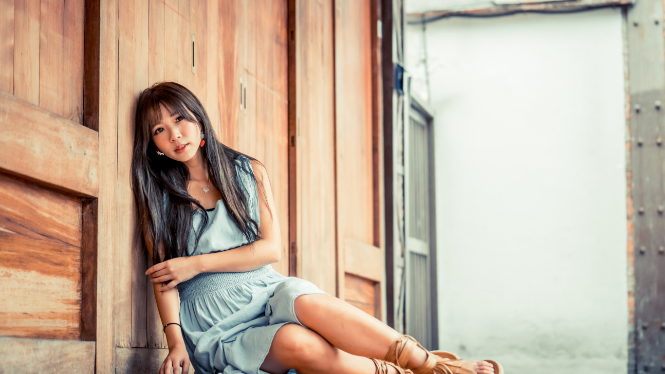 Девушка азиатка в платье сидит на полу у стены 