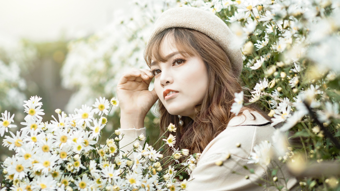 Девушка азиатка сидит в белых цветах ромашки 