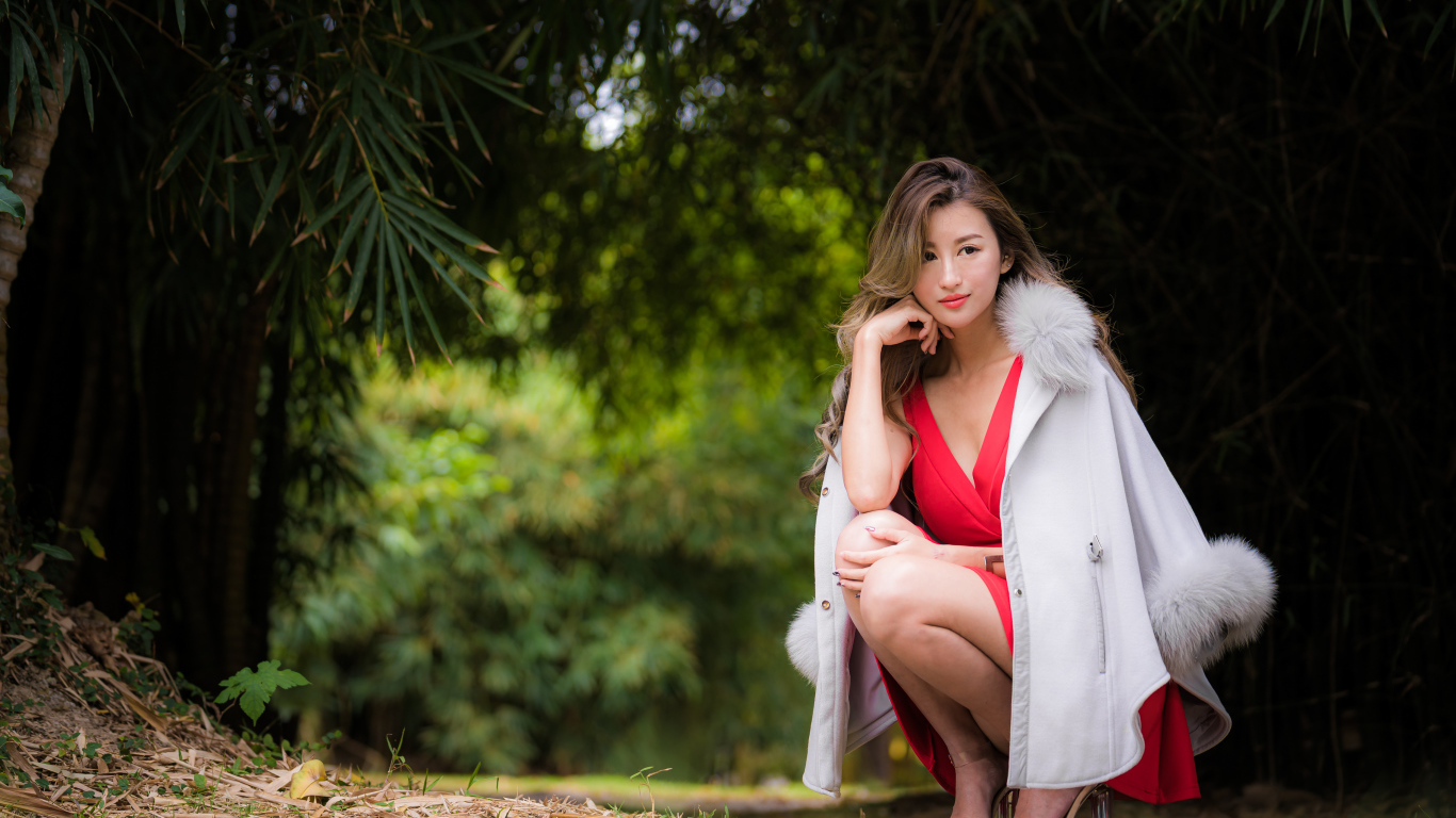 Азиатка в красном платье сидит в парке 