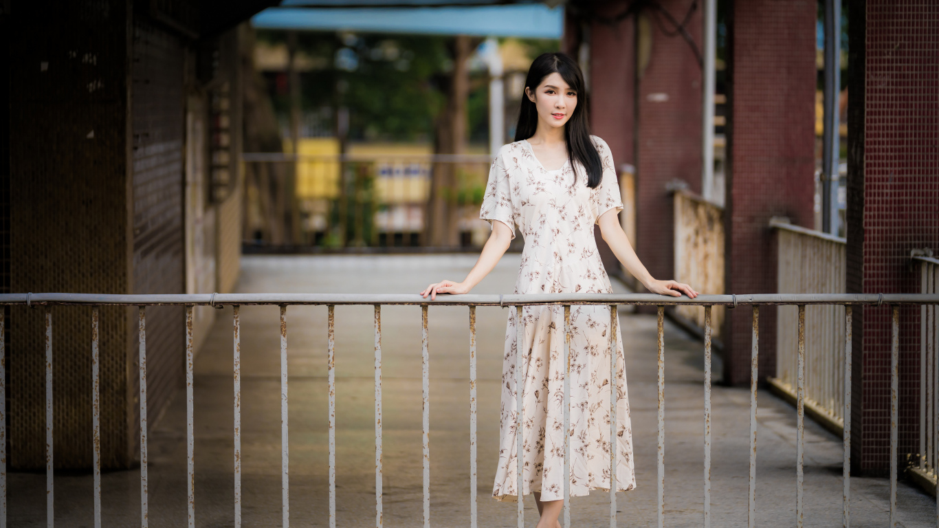 Красивая азиатка в платье стоит у перил