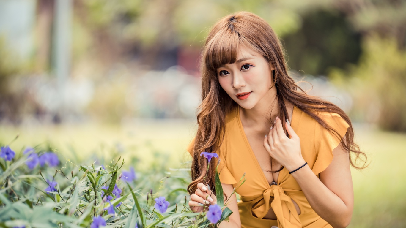 Красивая девушка азиатка в желтом платье у фиолетовых цветов 