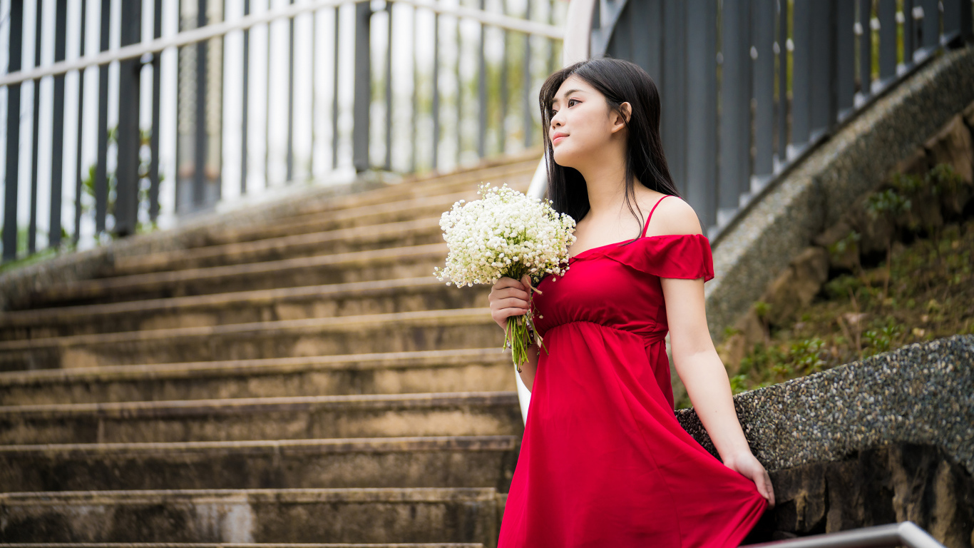 Красивая азиатка в красном платье стоит на ступеньках с букетом ландышей