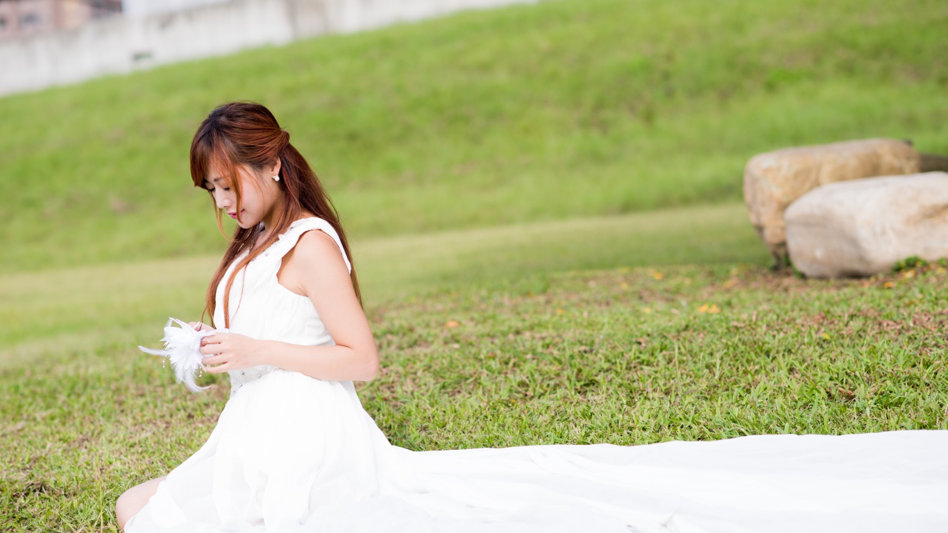 Красивая девушка азиатка в свадебном платье сидит на траве