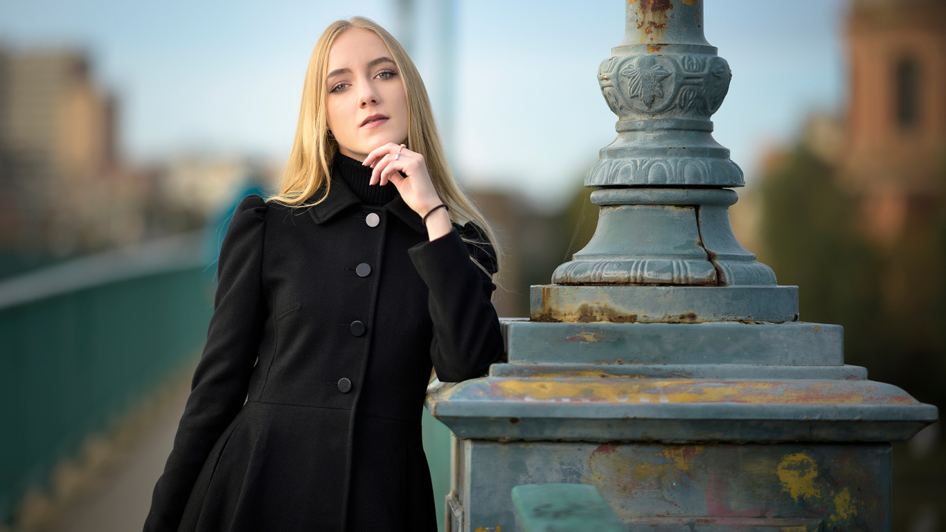 Красивая блондинка в черном пальто стоит у фонаря