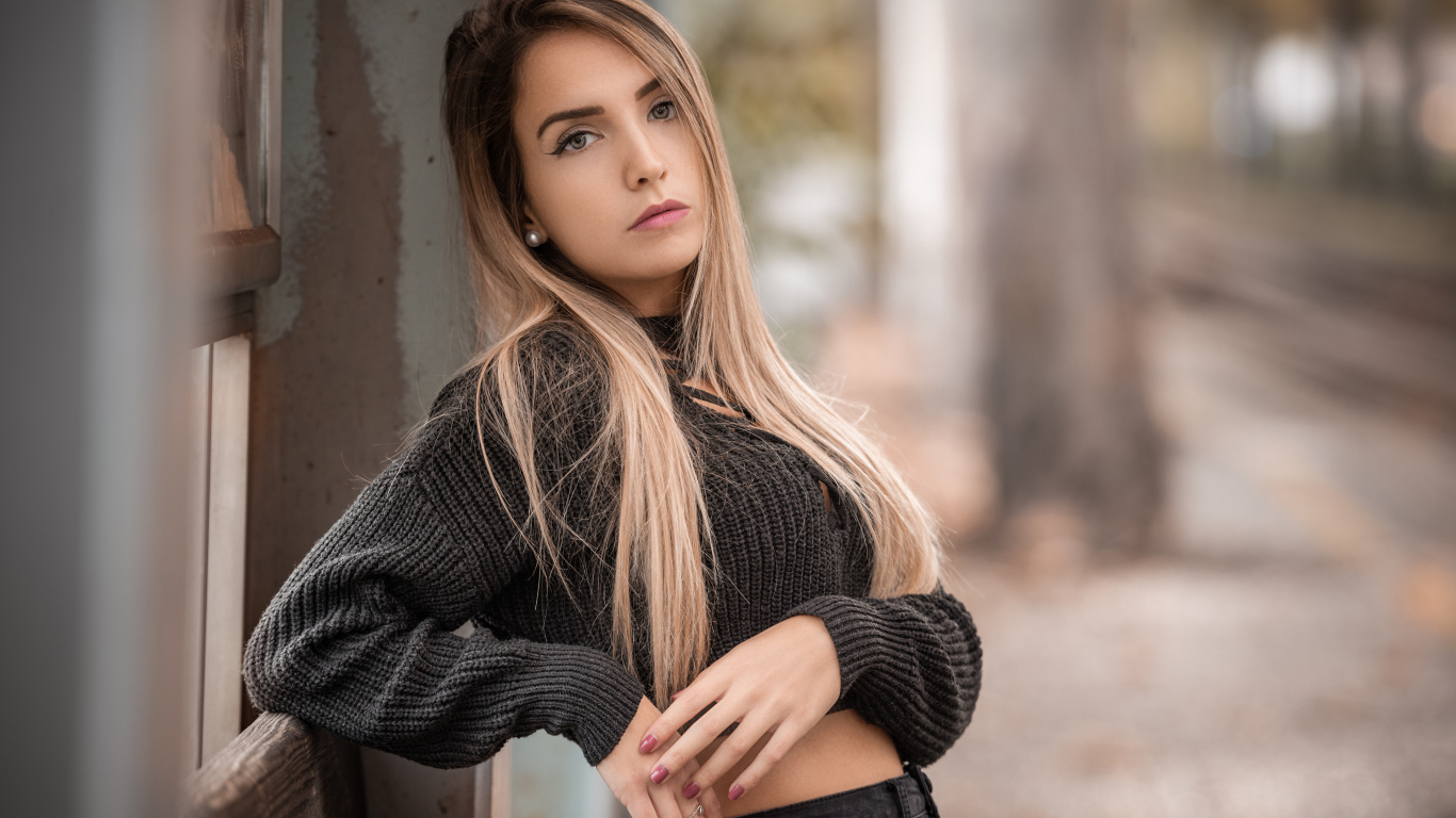 Красивая блондинка в вязаном свитере у стены 