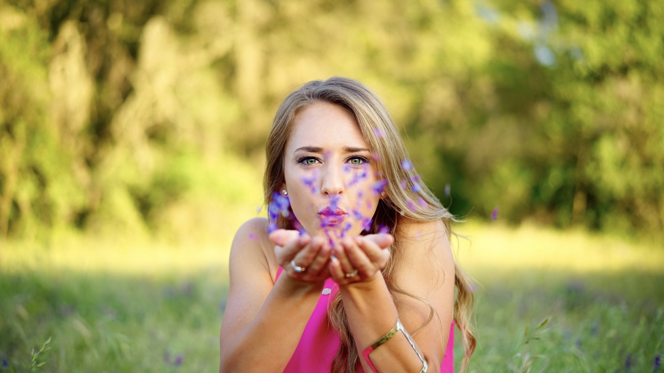 Красивая девушка сдувает лепестки с ладоней 